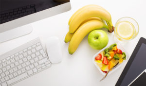 A desk with a computer, keyboard and mouse on accompanied with fruit